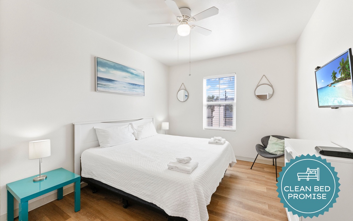Rest peacefully in your bright bedroom with coastal art, ceiling fan, and modern TV for your comfort.