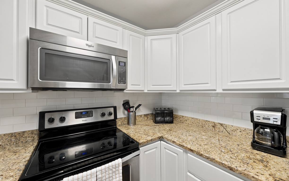This fully equipped kitchen features granite countertops, stainless steel appliances including microwave and stove, and bright white cabinetry with subway tile backsplash—everything you need to prepare your favorite meals during your stay.
