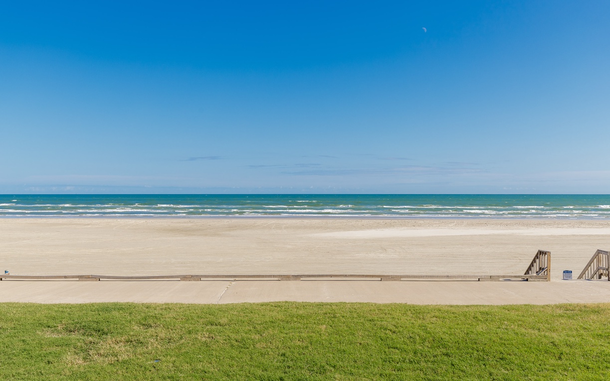 Pristine beachfront location with direct access to miles of sandy shoreline and rolling waves under clear blue skies.