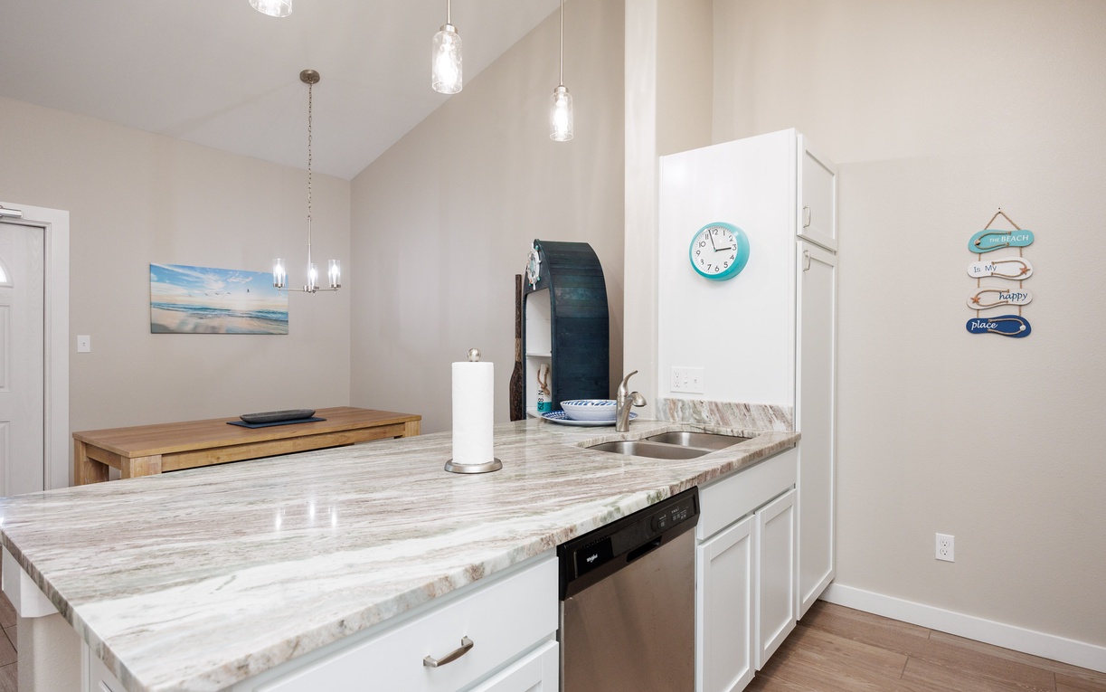 Your modern kitchen features gleaming marble countertops and sleek white cabinetry, perfect for preparing meals during your beach getaway.