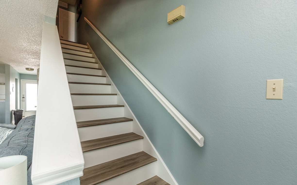Your private staircase awaits, featuring warm wood treads and crisp white railings that lead you to your upper-level retreat.