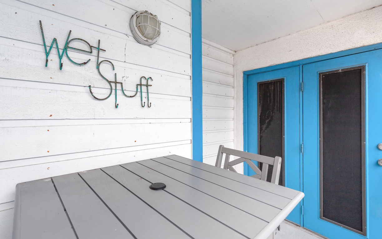 Your private patio offers coastal charm with comfortable outdoor dining and whimsical 'Wet Stuff' signage setting the perfect beach vibe.