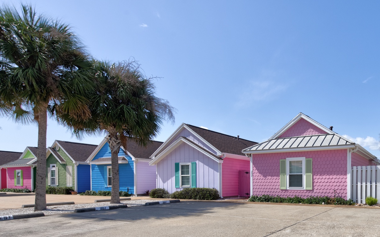Charming coastal cottages in vibrant colors line the property, creating a cheerful beachside atmosphere with tropical palm trees overhead.