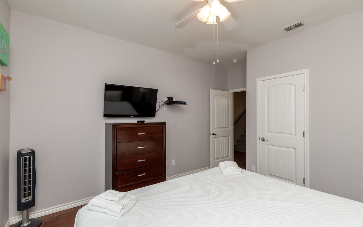 Unwind in your comfortable bedroom with plush linens, wall-mounted TV, and gentle ceiling fan for perfect sleeping temperatures.