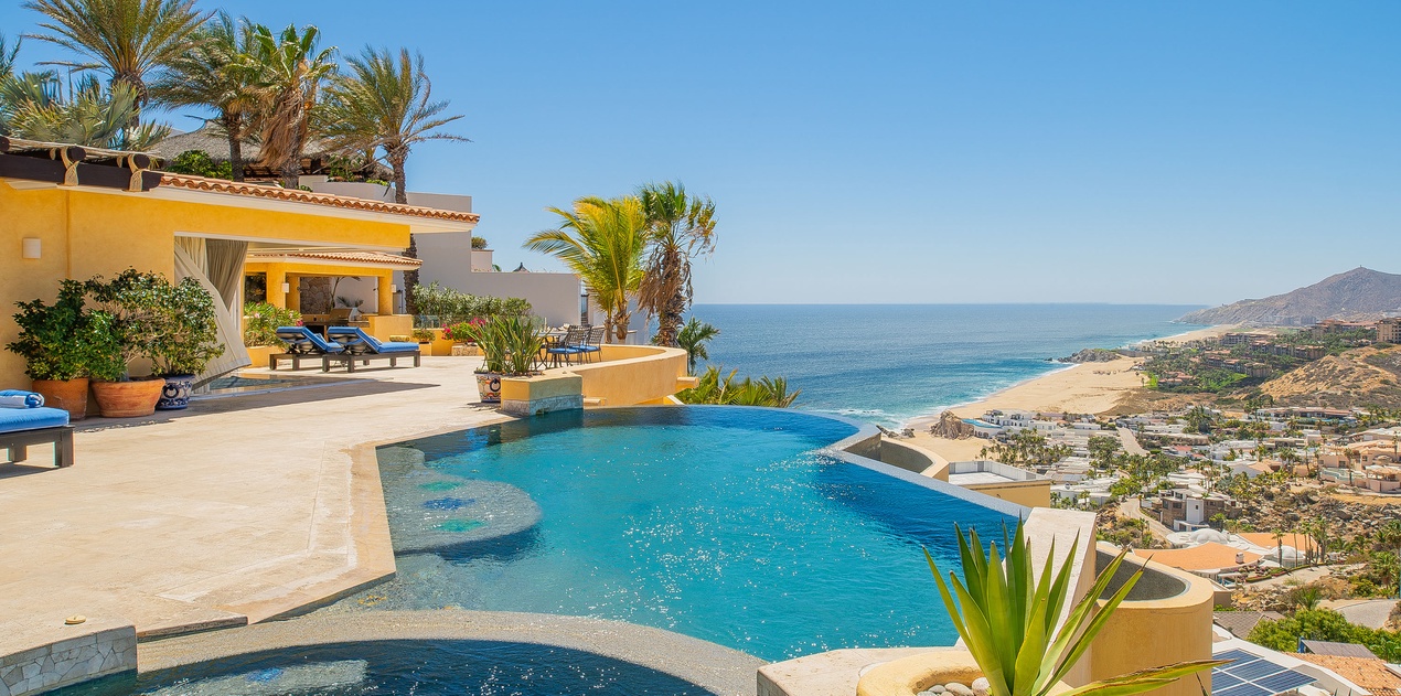 Stunning infinity pool overlooking azure waters and golden coastline, surrounded by tropical palms and luxurious outdoor lounging spaces.
