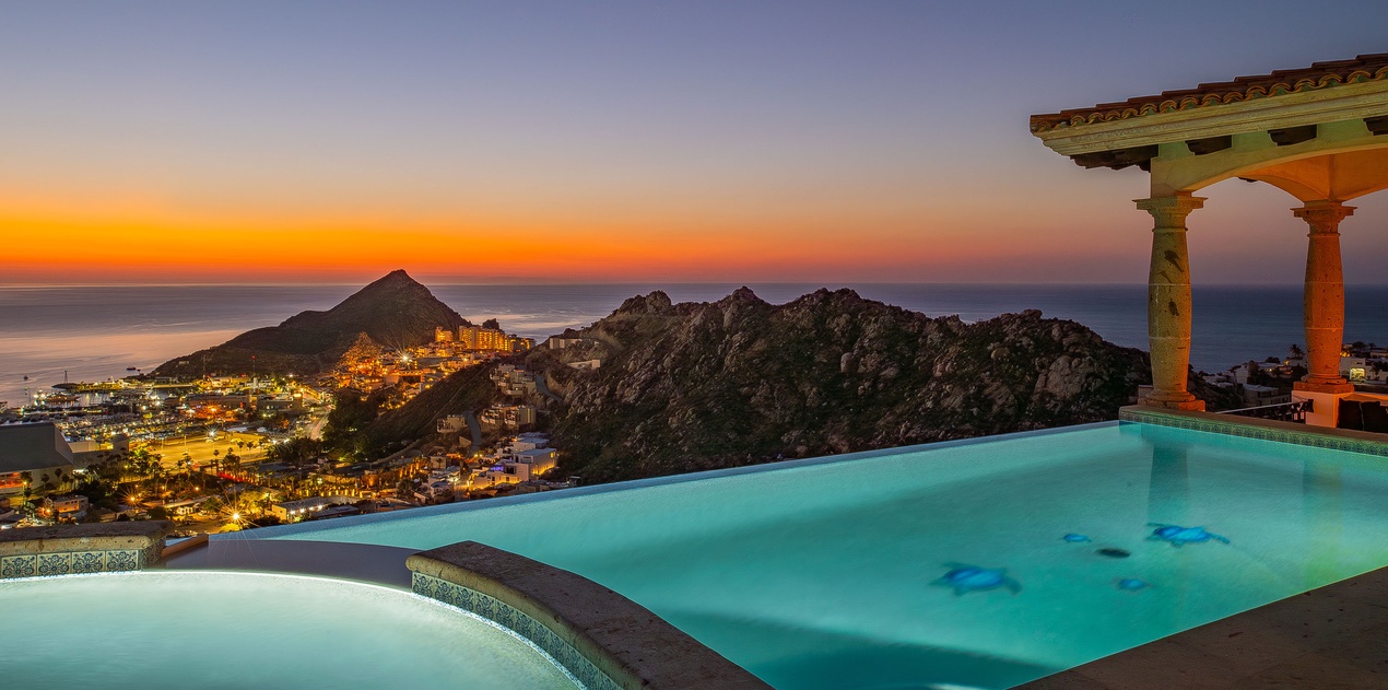Stunning infinity pool overlooks coastal mountains and city lights during golden sunset. Perfect evening setting with hot tub.