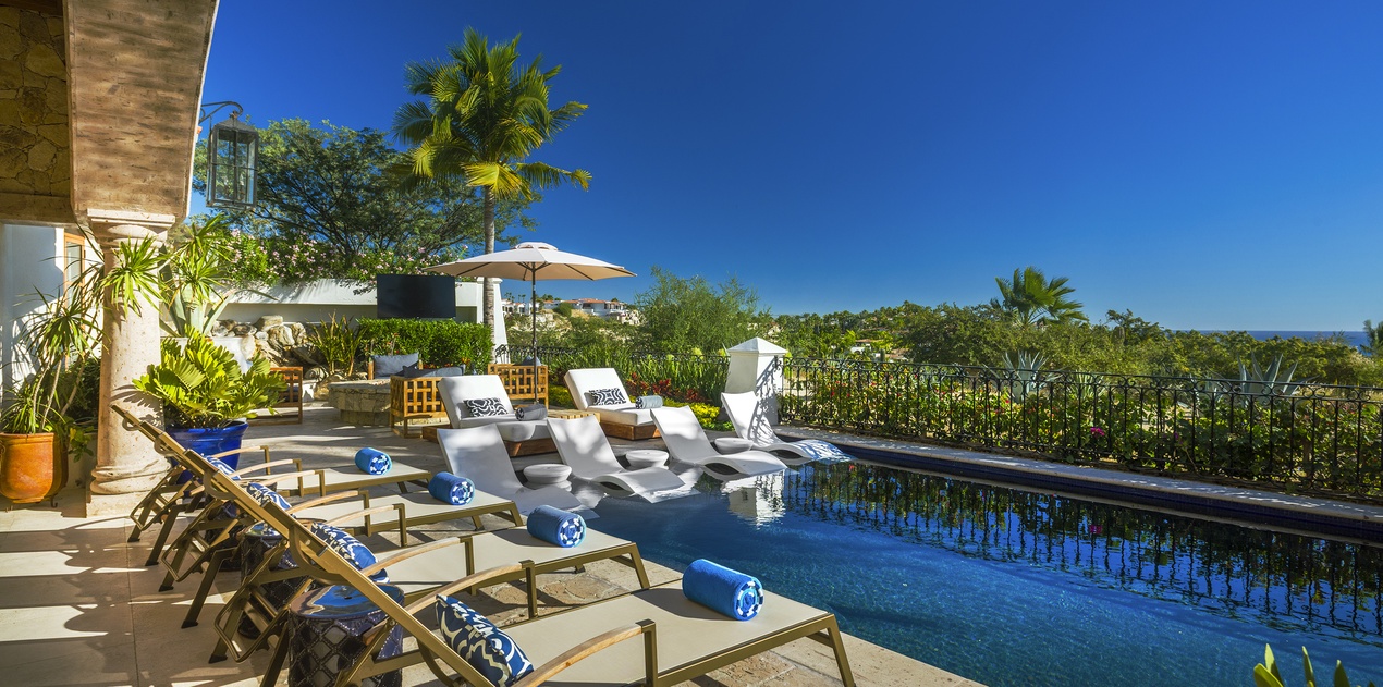 Luxurious infinity pool terrace with premium loungers overlooking lush tropical gardens under endless blue skies.