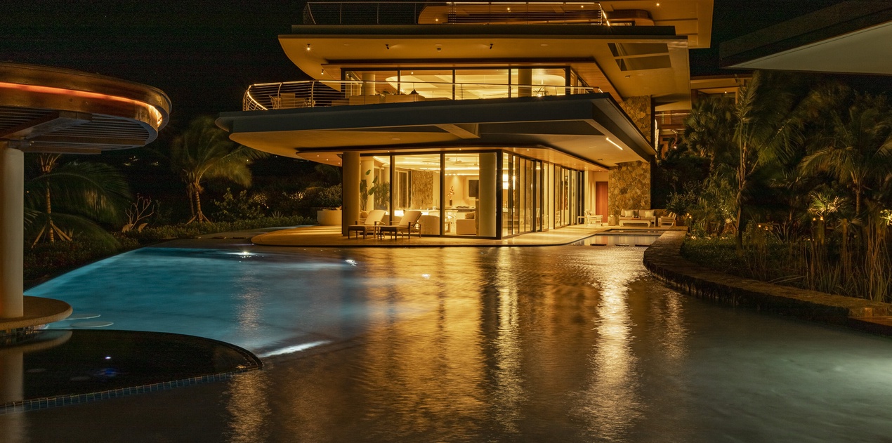 Modern luxury villa showcasing contemporary architecture with illuminated pool and tropical landscaping during evening hours.