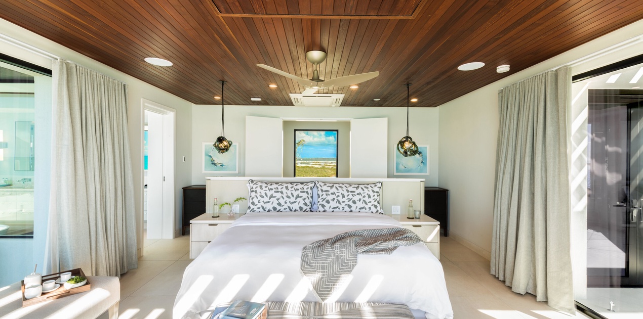 Sink into crisp linens under a stunning wood-paneled ceiling, where coastal artwork and soft natural light create your serene island retreat.