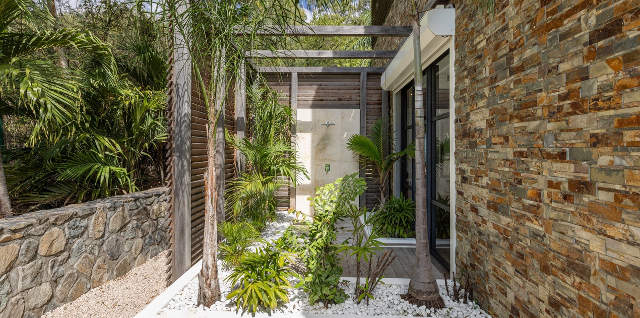 Modern tropical entrance with natural stone walls and lush landscaping creates a serene arrival experience.