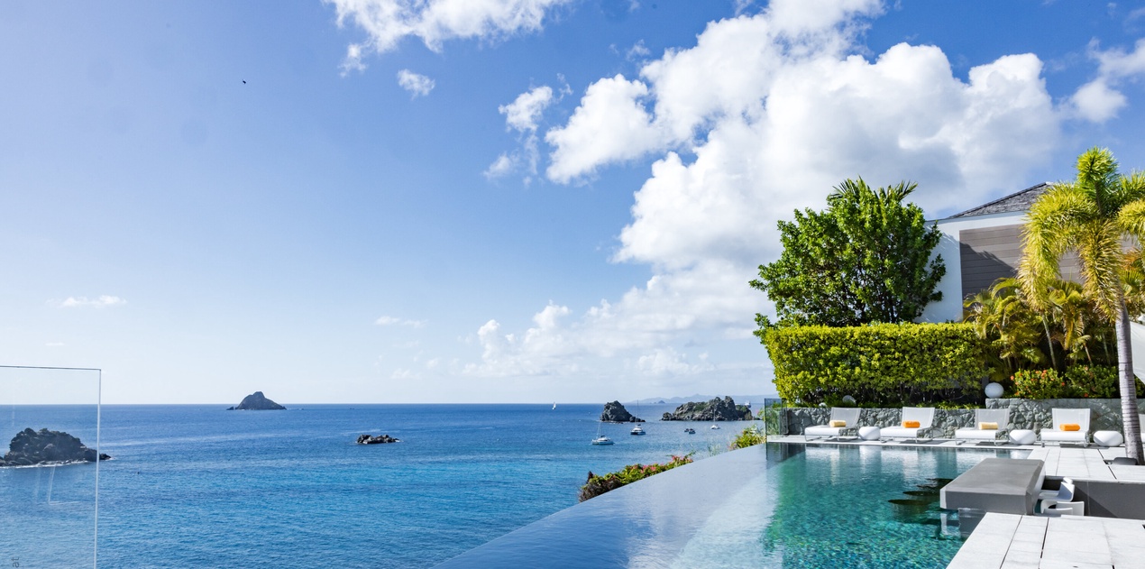 Stunning infinity pool overlooking pristine Caribbean waters with tropical landscaping and modern outdoor seating areas.