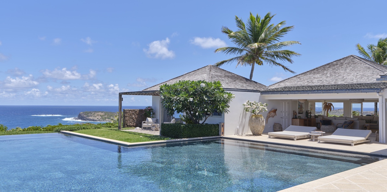 A stunning oceanfront villa with an infinity pool stretching toward endless blue waters. Swaying palms and open-air lounging areas frame your private tropical paradise.