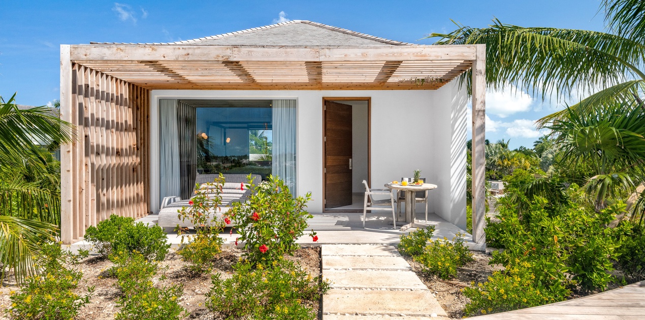 Modern tropical villa with pergola and private terrace surrounded by lush landscaping and palm trees.
