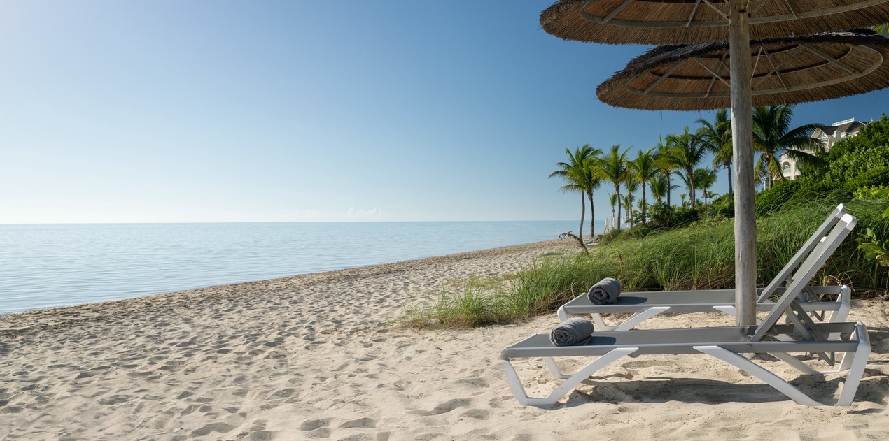 Private beach with lounge chairs and umbrellas, surrounded by swaying palm trees and pristine sand.