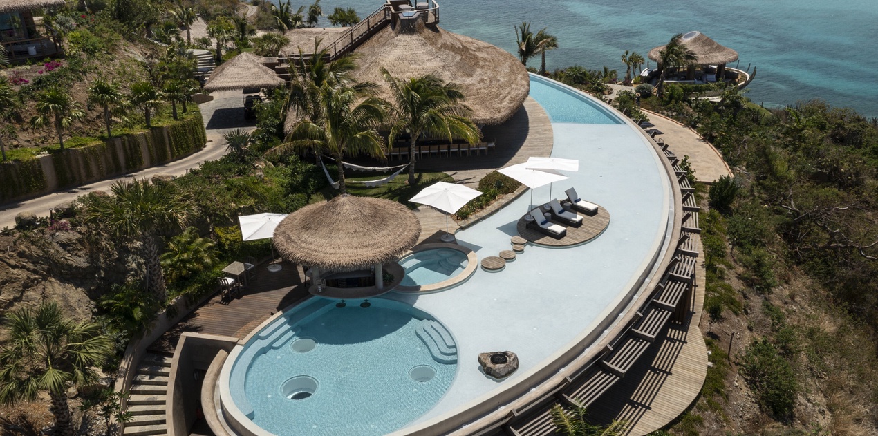 Stunning beachfront resort featuring an infinity pool with swim-up bar, surrounded by tropical palms and crystal-clear ocean views.