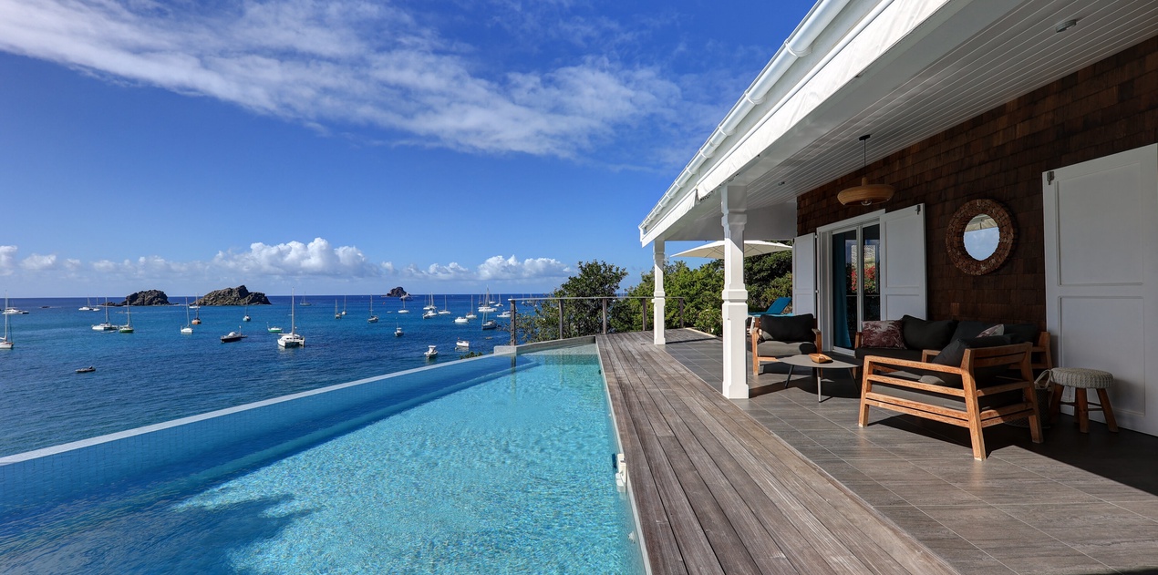 Stunning infinity pool overlooking crystal-clear Caribbean waters with boats dotting the horizon. Modern tropical paradise.
