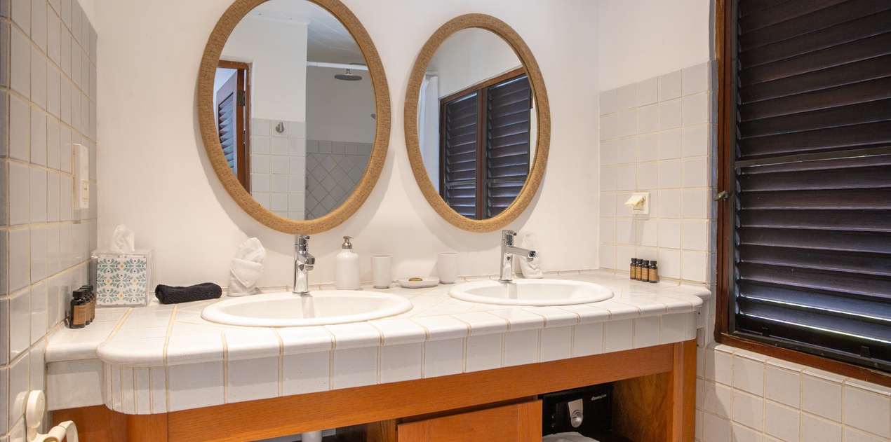 Start your morning refreshed at the dual vanities—elegant oval mirrors, white tile accents, and thoughtful touches like fresh towels and island-style shutters create your serene retreat.