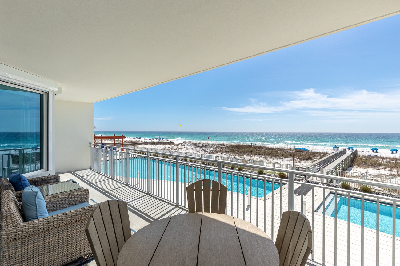 Relax on your private balcony with stunning ocean views, poolside dining table, and comfortable seating overlooking pristine beach.