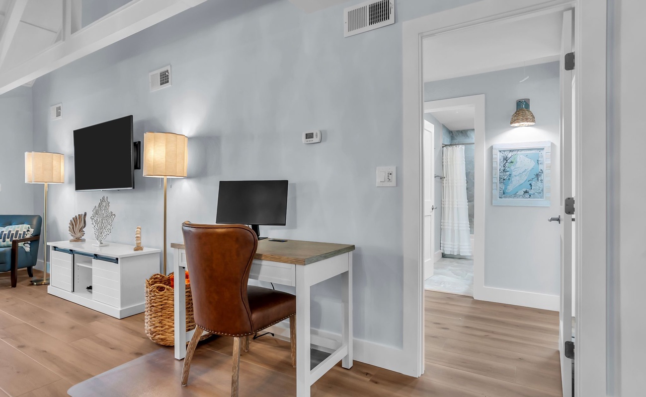 A thoughtfully designed workspace tucked into the living area, featuring a sleek desk, leather chair, and soft coastal hues that create a calm and productive atmosphere.