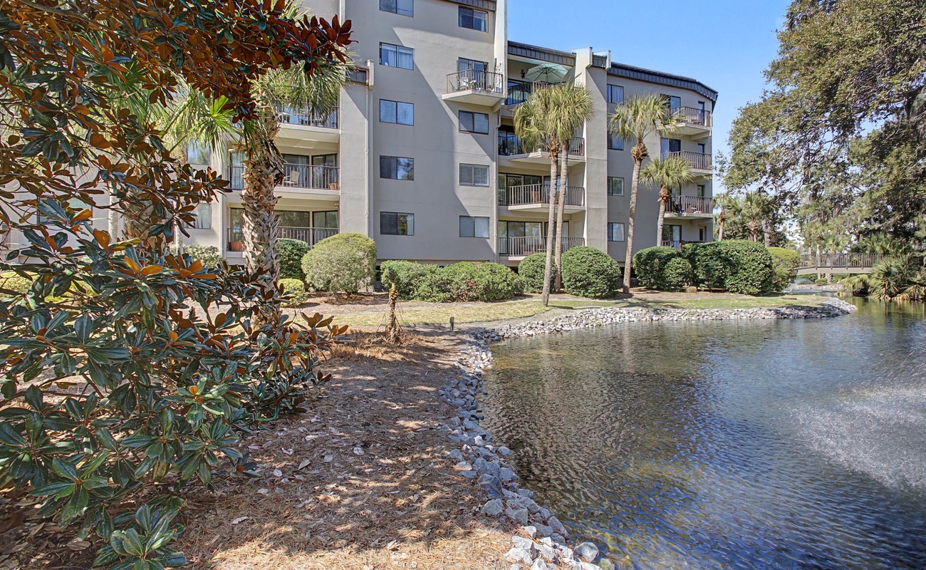 Multi-story waterfront property featuring private balconies and tropical landscaping along a peaceful water feature.
