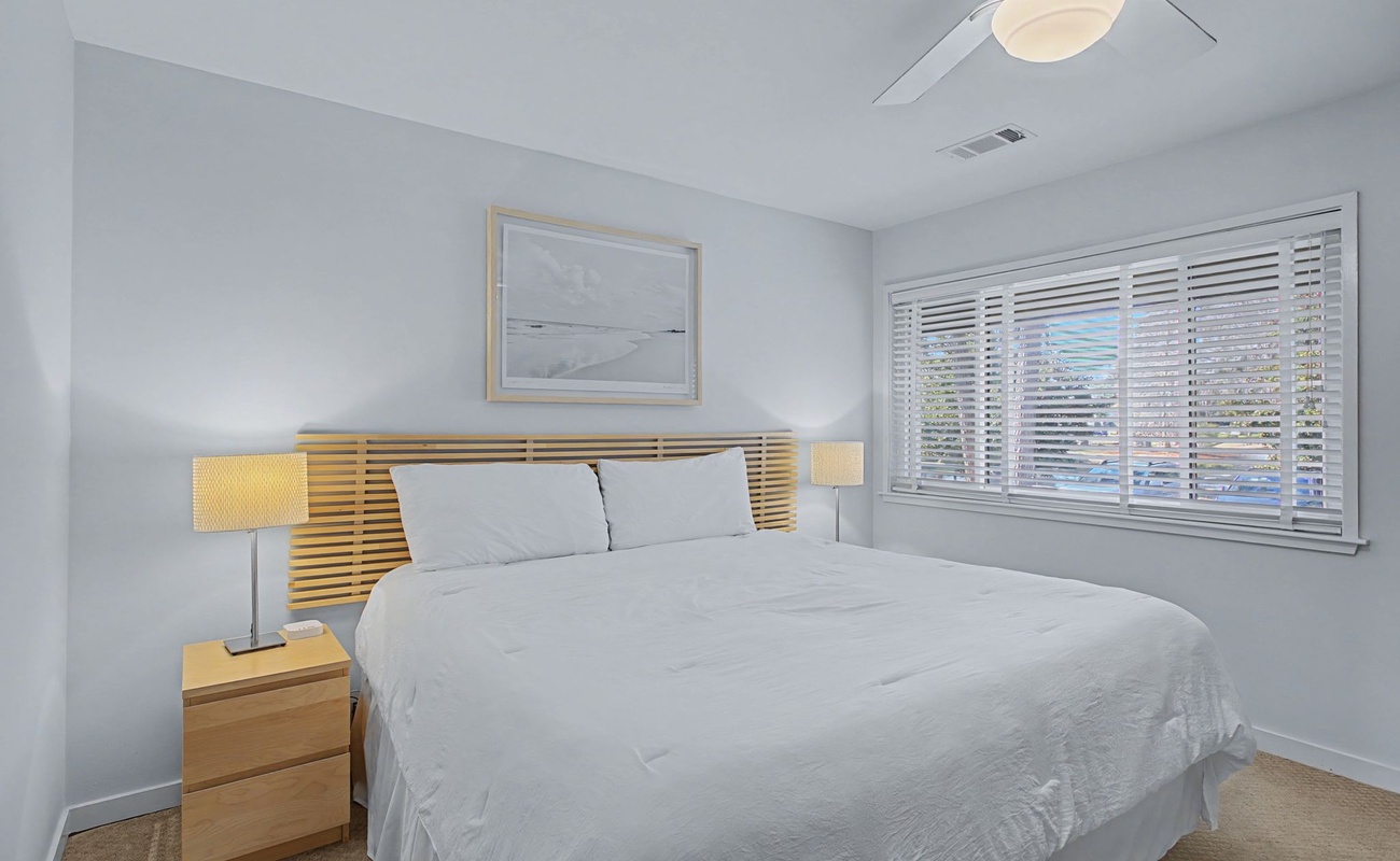 Rest peacefully in your modern bedroom featuring crisp white linens, a warm wood headboard, and natural light filtering through window blinds.