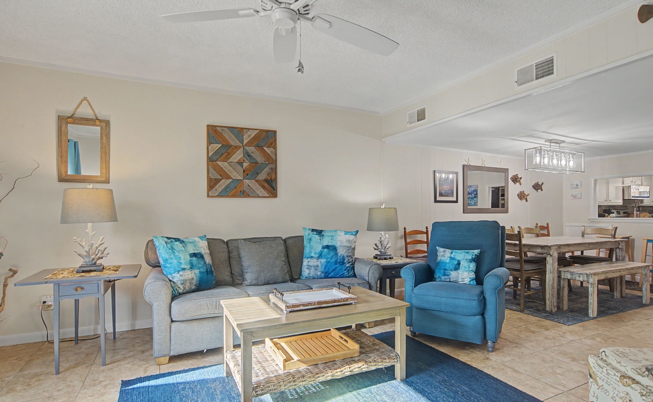 Relax in your open-concept living space with coastal-inspired decor, comfortable seating, and a cooling ceiling fan overhead.