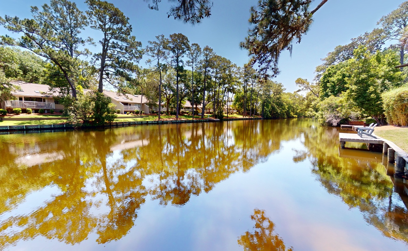 Peaceful pond surrounded by towering trees and waterfront property buildings with private dock access for a tranquil retreat experience.