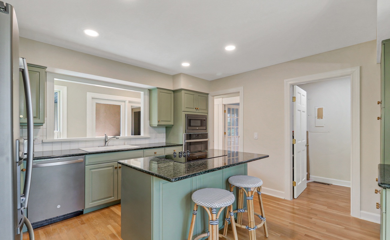 Your fully equipped kitchen features sage green cabinetry, granite countertops, and modern appliances, perfect for preparing meals during your stay.