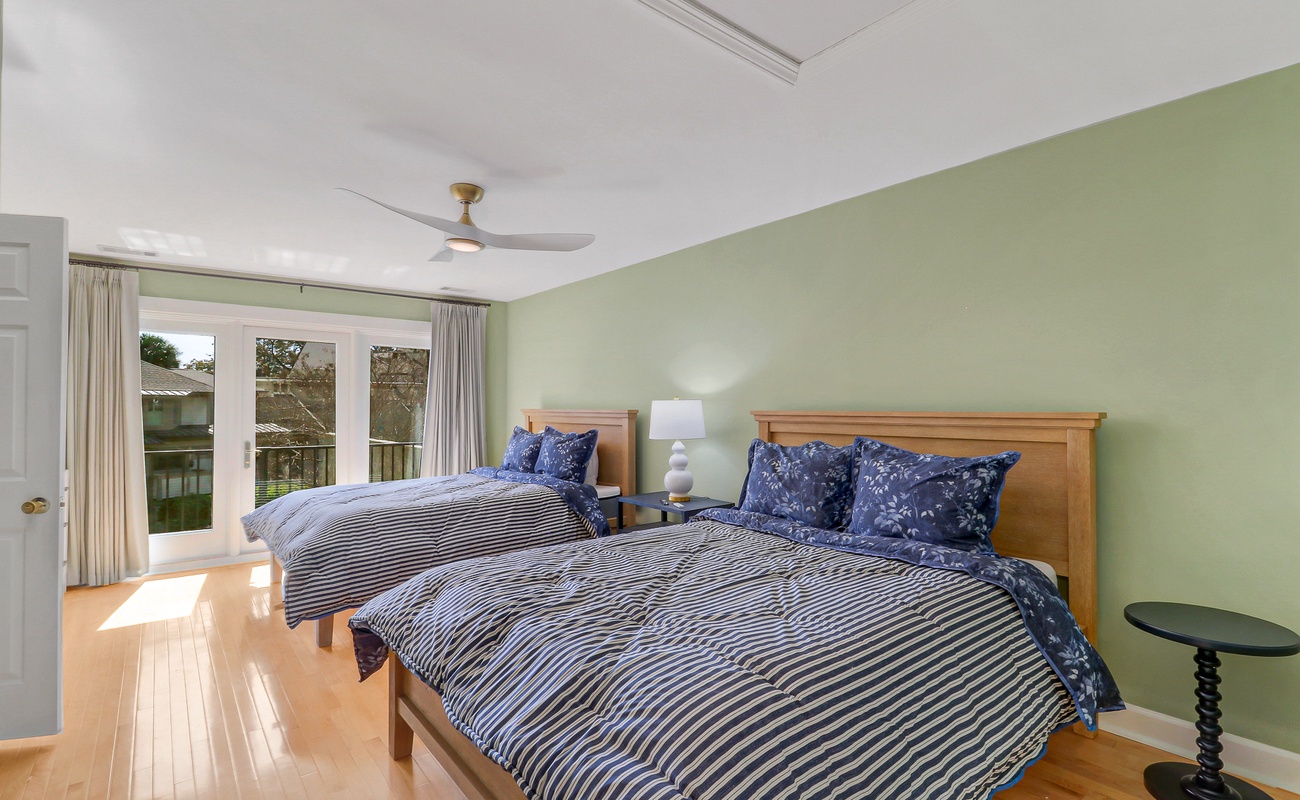 Unwind in your peaceful twin bedroom with fresh green walls, polished hardwood floors, and French doors opening to nature views.