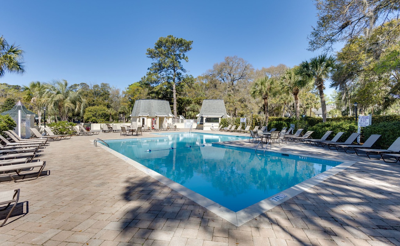 Beautiful community swimming pool surrounded by palm trees and tropical landscaping with comfortable lounge chairs.