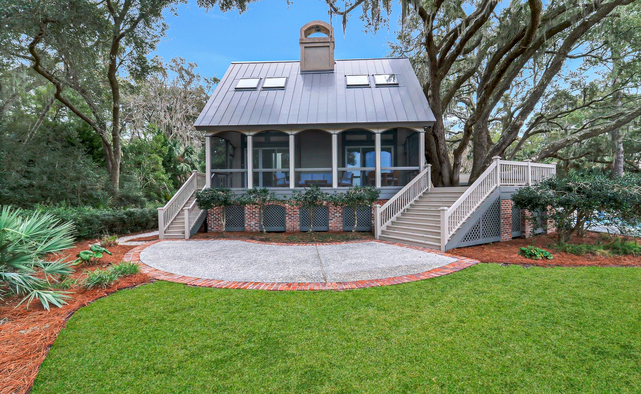 Charming cottage nestled among towering oaks with welcoming front porch and beautifully landscaped grounds surrounded by lush natural beauty.