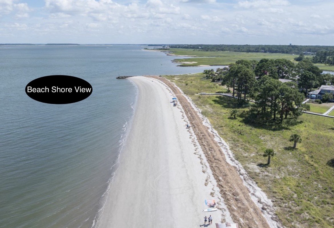 Aerial view of pristine sandy beach stretching along calm waters, with lush coastal landscape and nearby amenities.