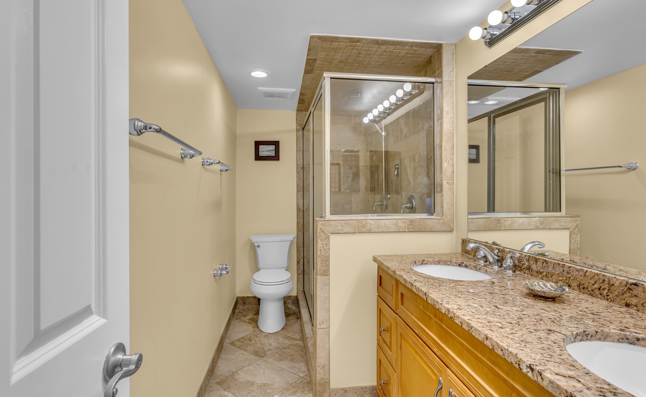 Unwind in this elegant bathroom featuring granite countertops, dual vanities, and a spacious glass-enclosed shower for your comfort.