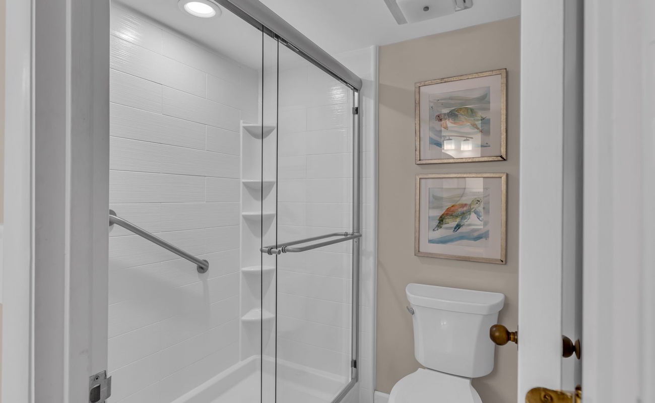 Step into your private sanctuary with a gleaming glass-enclosed shower and thoughtful coastal artwork that sets a serene, spa-like mood.