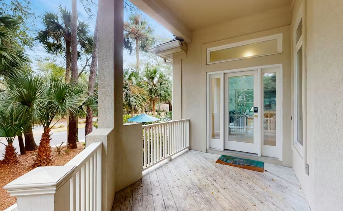 Step onto your private covered porch where tropical palms frame peaceful pool views through elegant railings.
