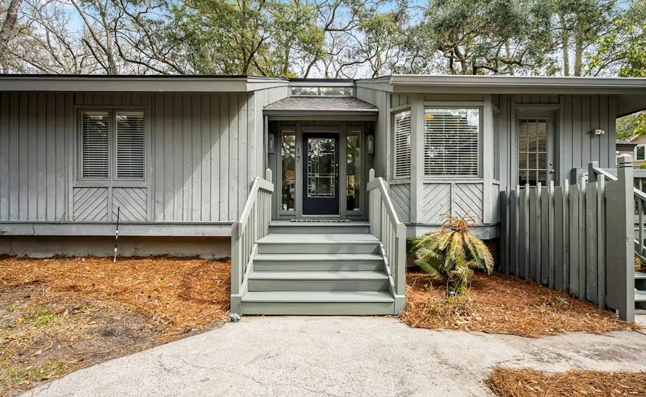 A charming coastal retreat with natural wood siding and welcoming front entrance, nestled among mature trees for privacy and tranquility.