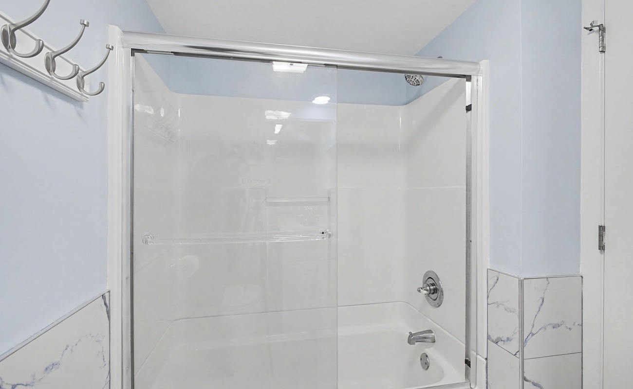 Step into your beautifully appointed bathroom featuring a spacious glass-enclosed shower with elegant marble-look tiling and chrome fixtures for your refreshing moments.