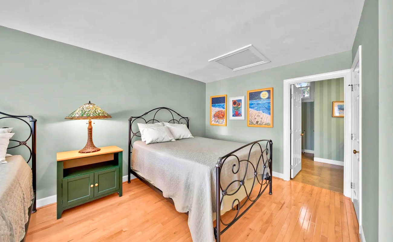Drift off to sleep in your peaceful bedroom featuring vintage iron beds, warm hardwood floors, and charming coastal artwork on calming sage walls.