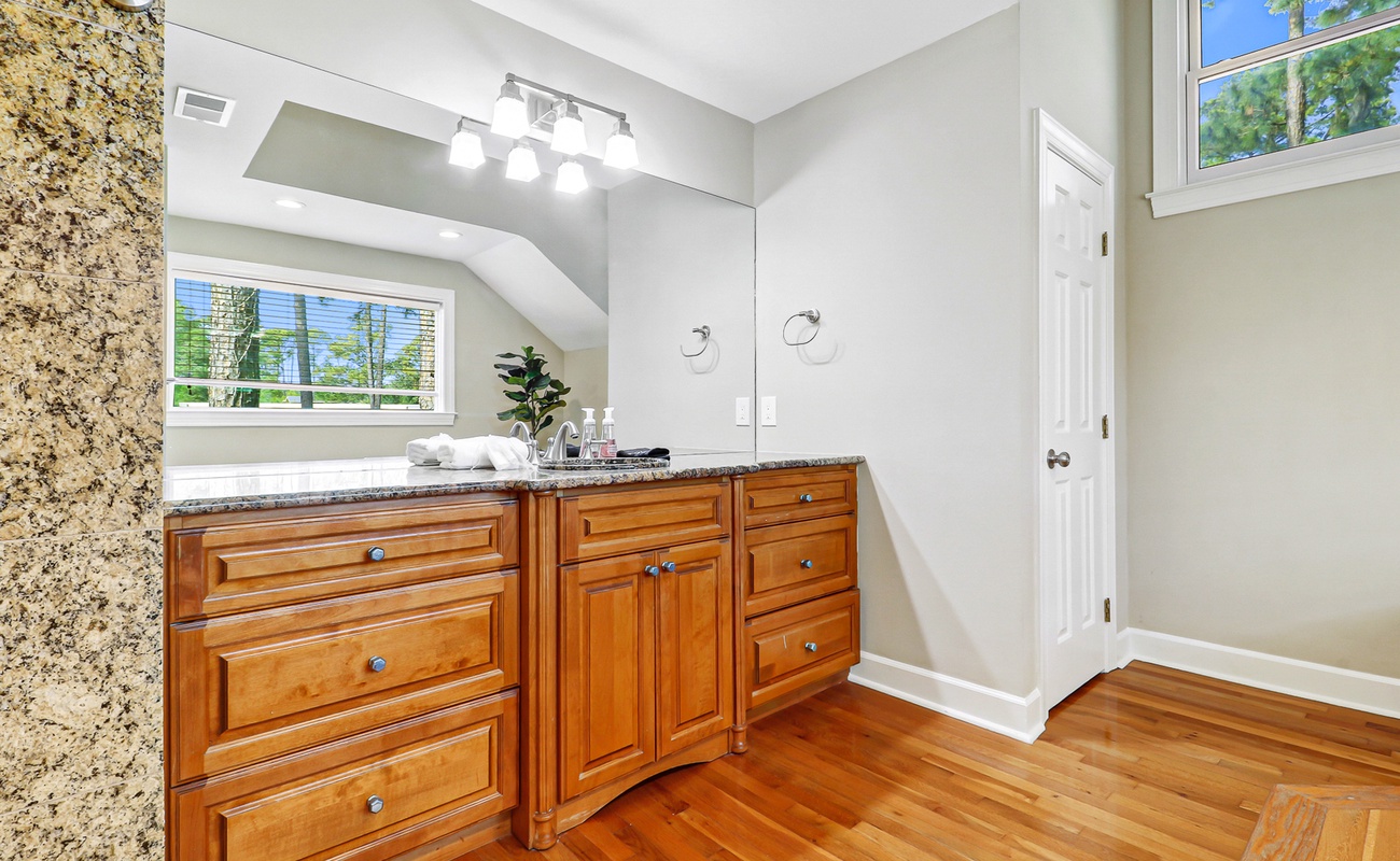 Refresh in this elegant bathroom featuring granite countertops, warm wood cabinetry, and bright natural light streaming through the windows.