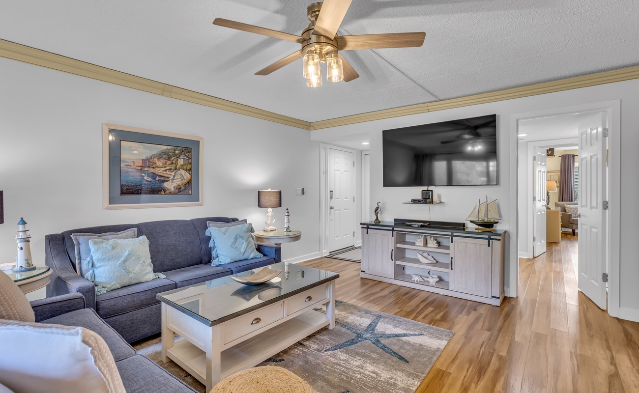 Relax in your coastal-inspired living room with plush seating, elegant ceiling fan, and entertainment center—perfect for unwinding after beach days.