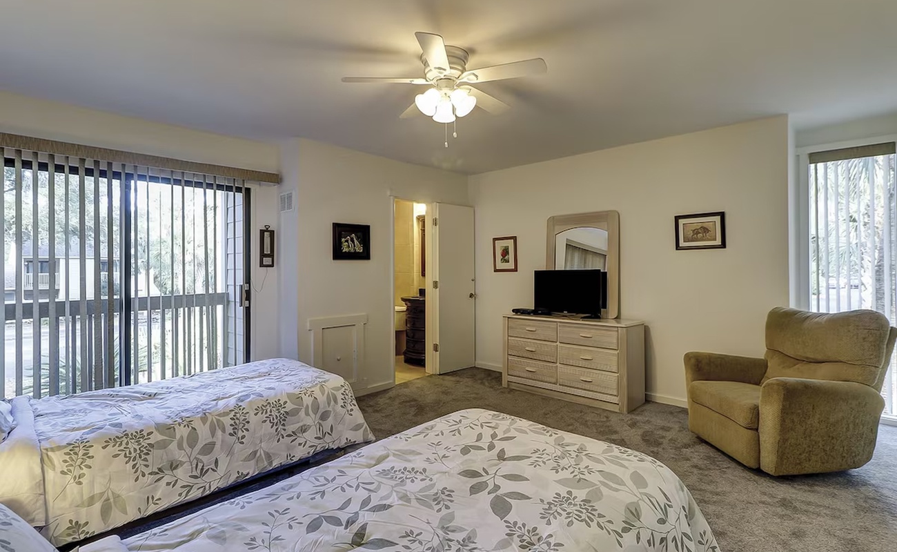 Unwind in your spacious bedroom featuring twin beds, cozy armchair, and private patio access for peaceful mornings.