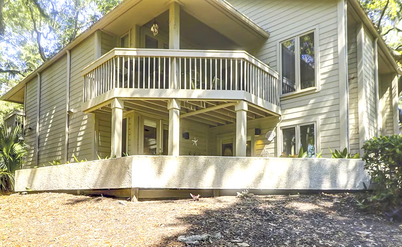 A charming two-story vacation rental nestled among mature trees, featuring a covered ground-level patio and upper balcony perfect for relaxing.