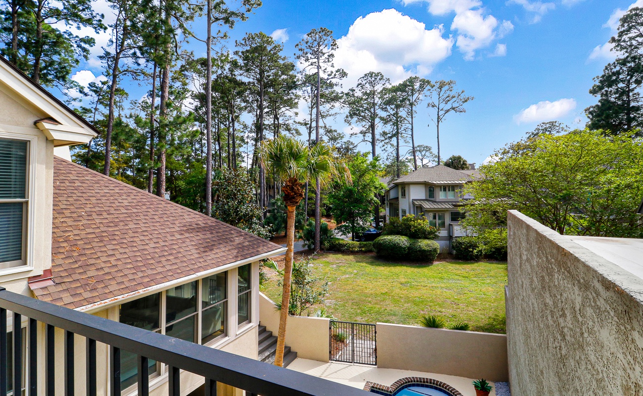 A peaceful residential property nestled among tall pines with well-maintained grounds and neighboring homes visible in the distance.