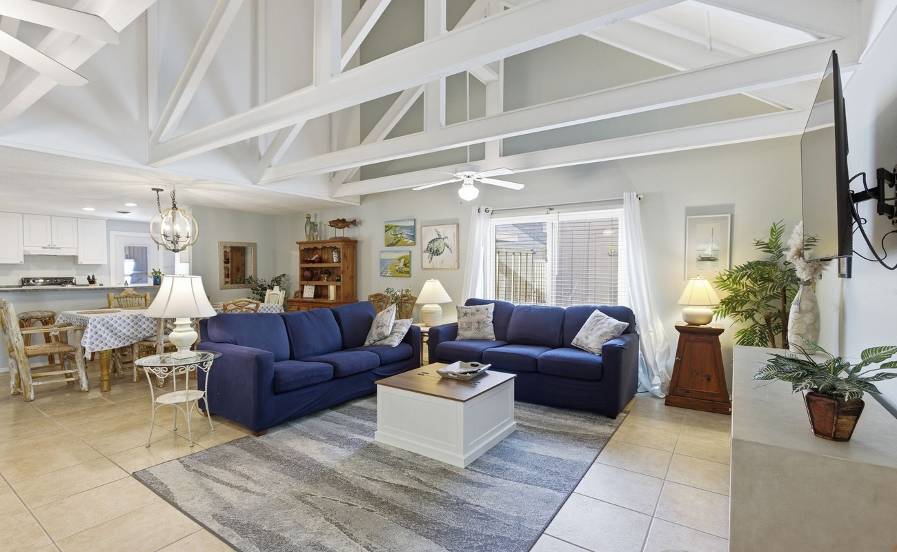 Relax in your spacious living room featuring exposed white beams, navy sectional seating, and coastal touches throughout this bright, airy space.