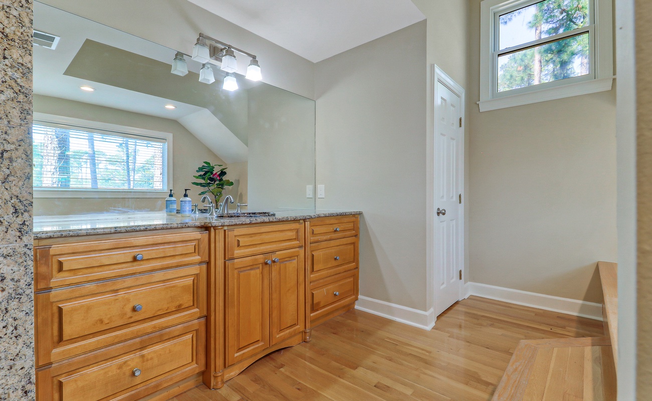 Pamper yourself in this elegant bathroom with warm wood cabinetry, granite countertops, and natural light streaming through windows.