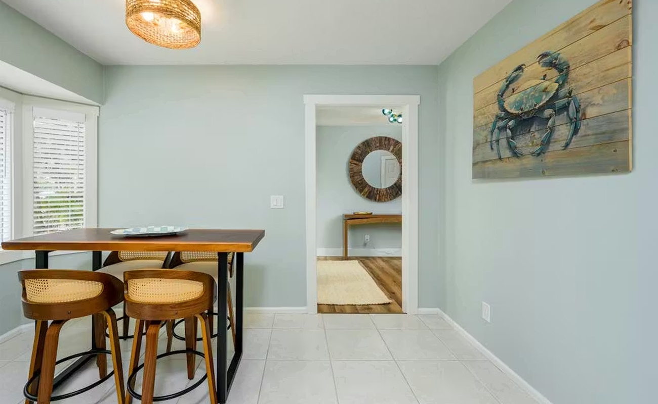 Gather around your stylish dining table beneath warm wicker lighting, where coastal charm meets modern comfort in this inviting space.