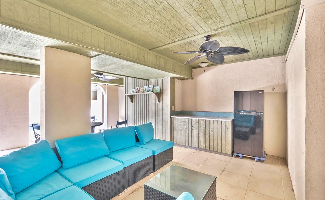 Unwind in your private covered patio featuring plush turquoise seating, ceiling fan, and outdoor kitchen—perfect for morning coffee or evening relaxation.