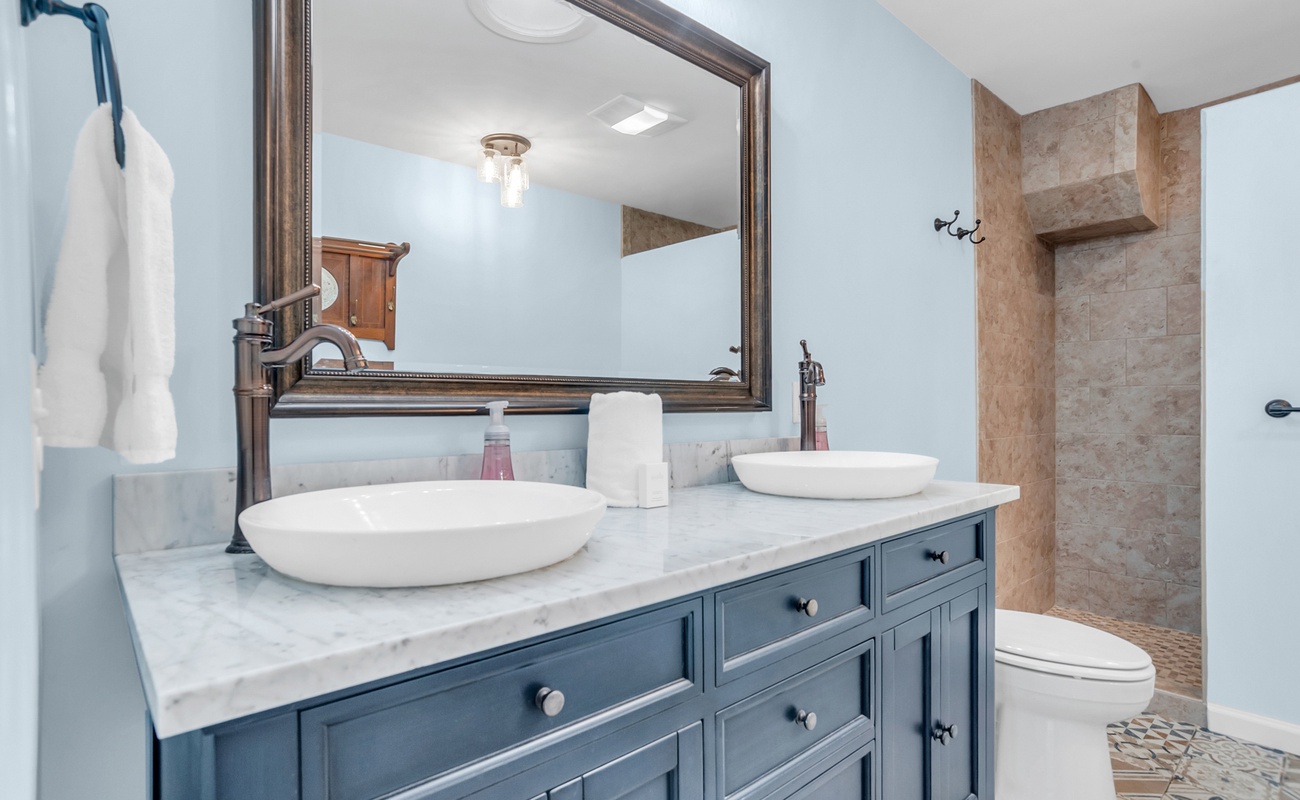 Unwind in your elegant bathroom featuring marble countertops, dual vessel sinks, and a luxurious stone-tiled shower for your perfect getaway.