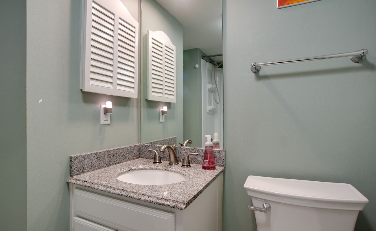 Your private bathroom features granite countertops, white cabinetry, and soothing mint green walls that create a refreshing coastal vibe.