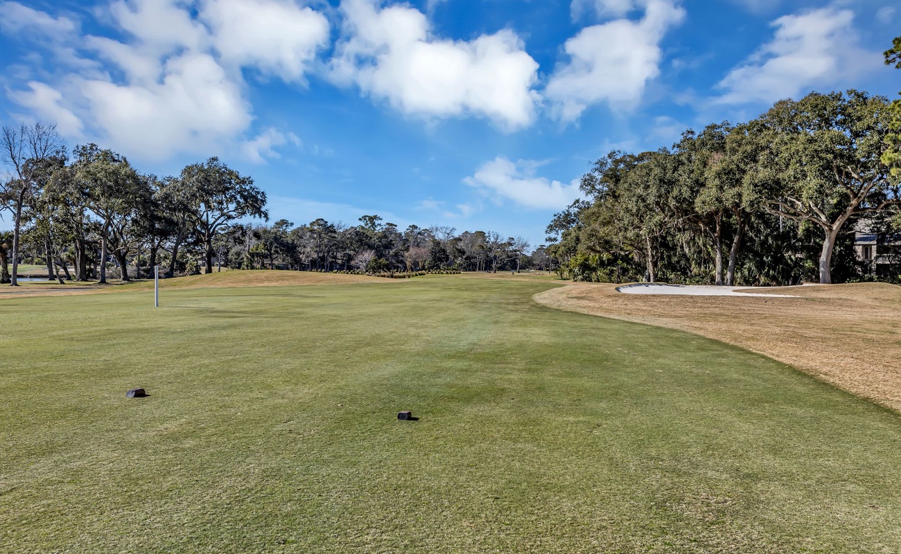 Pristine golf course with manicured greens surrounded by mature trees under a brilliant blue sky.